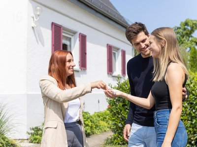 Immobilienmaklerin übergibt jungem Paar Hausschlüssel